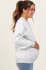 woman wearing a light gray oversized maternity sweatshirt and holding her baby bump, side profile view