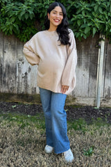 woman wearing a beige oversized maternity sweater with a baby bump and blue flared jeans