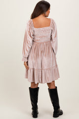 woman wearing a blush pink maternity dress with smocked bodice and long sleeves, standing with her back to the camera