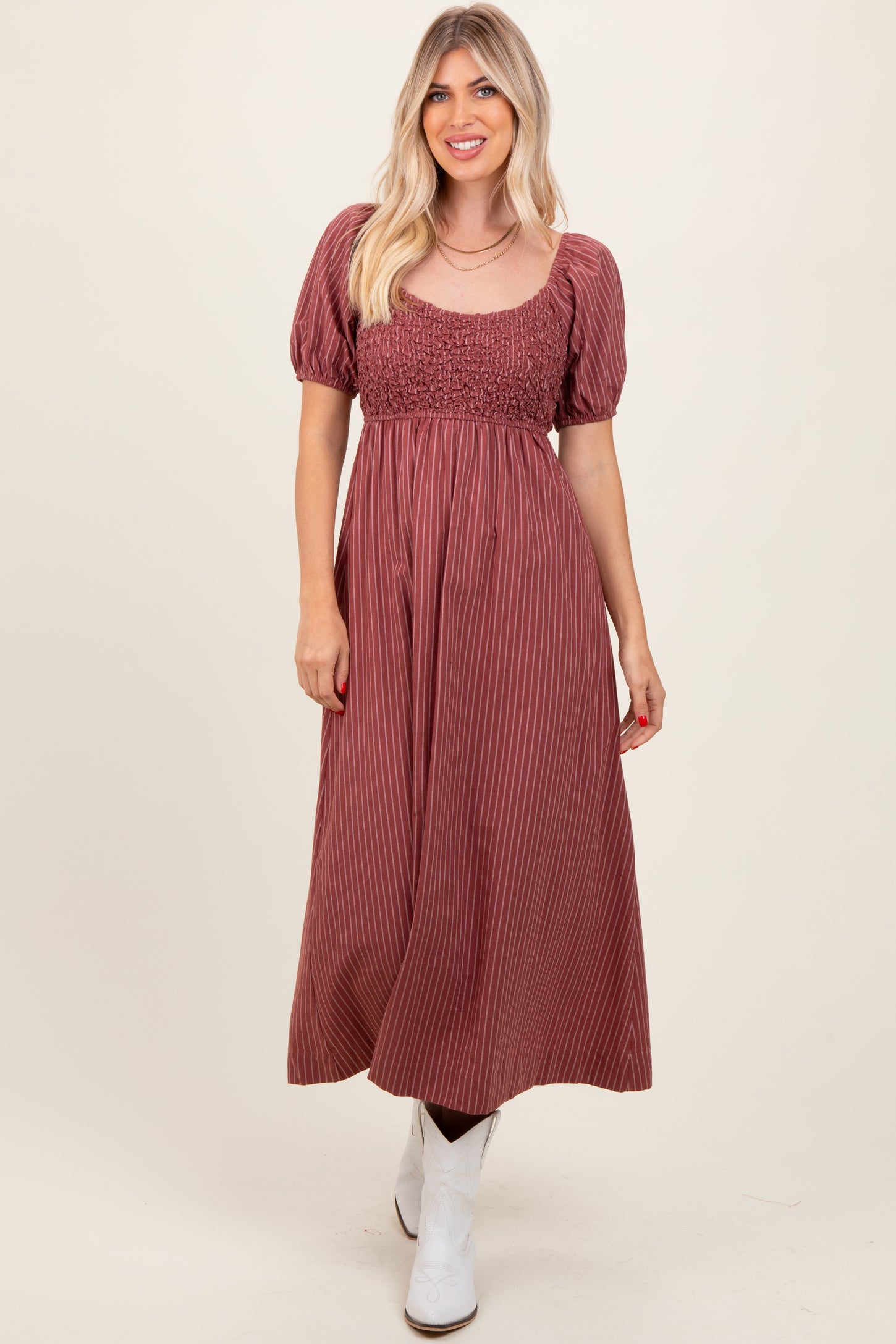 woman wearing a burgundy striped maxi dress with a smocked bodice and puff sleeves, paired with white ankle boots