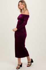woman wearing a fitted burgundy off-the-shoulder dress with long sleeves and a midi length, paired with black sandals