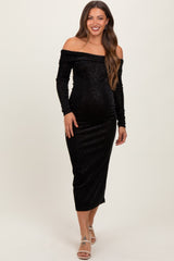 woman wearing a black off-the-shoulder maternity dress with long sleeves and a fitted silhouette, showing her baby bump