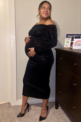 woman wearing a black off-the-shoulder maternity dress showing her baby bump while standing next to a dresser