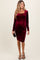 woman wearing a burgundy long sleeve velvet maternity dress with ruched details and a baby bump visible