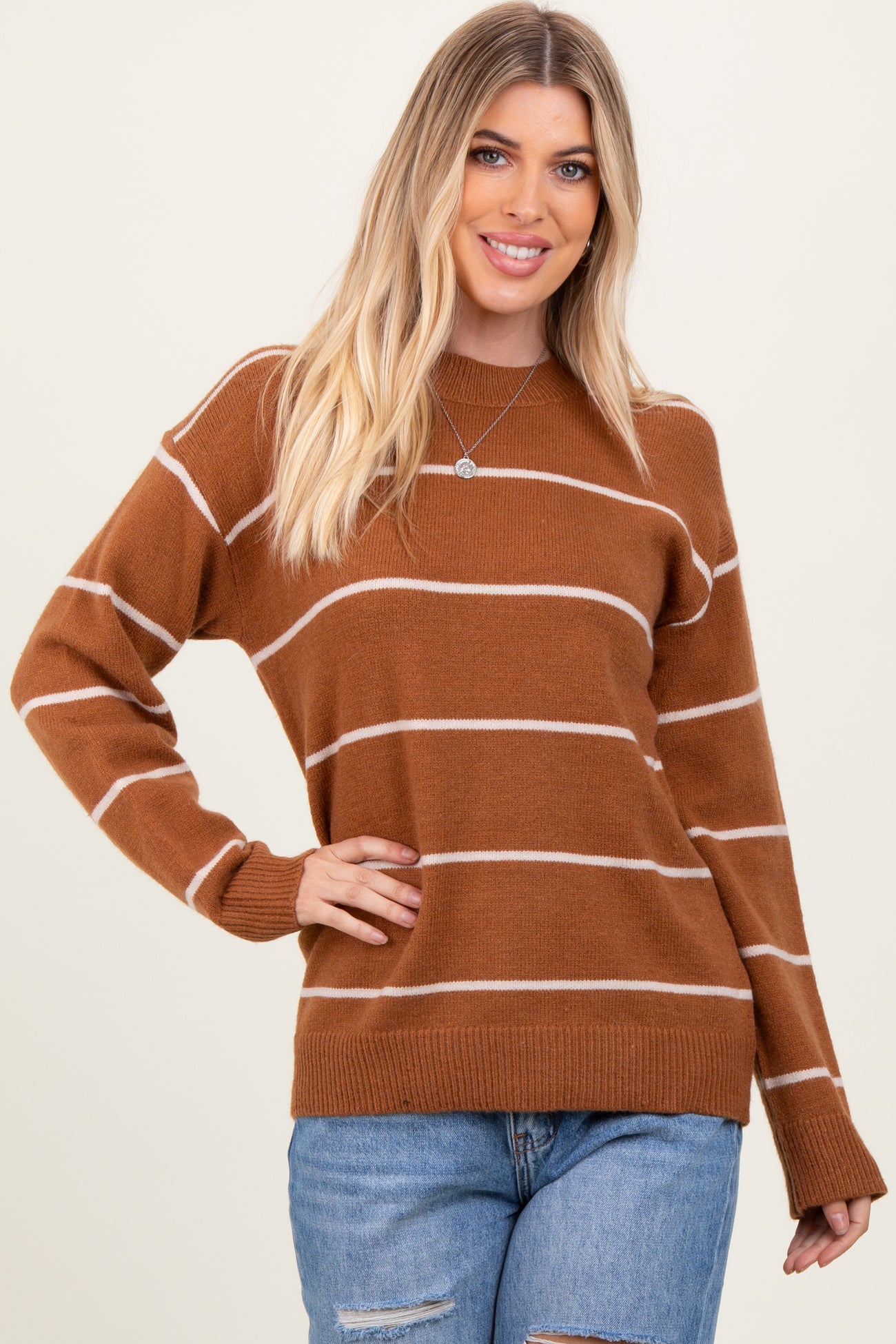 woman wearing a brown striped sweater with a crew neckline and long sleeves, paired with distressed denim jeans