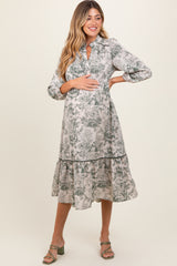 woman wearing a floral print maternity dress with a tiered skirt and a keyhole neckline, cradling her baby bump