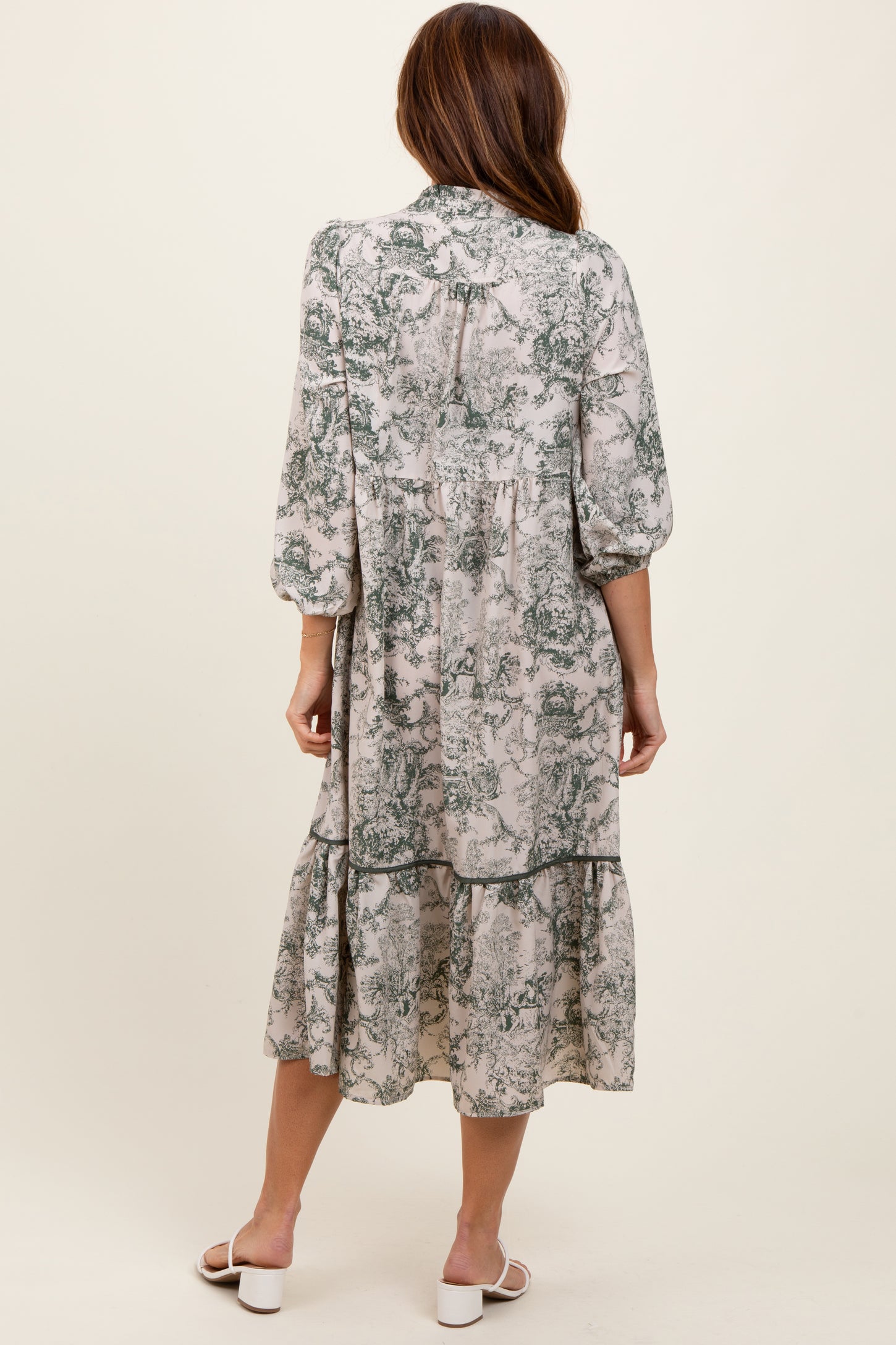 woman wearing a long, flowy gray and green floral midi dress with puff sleeves and a tiered skirt, seen from the back