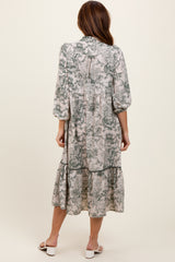 woman wearing a long, flowy gray and green floral midi dress with puff sleeves and a tiered skirt, seen from the back