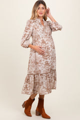 woman wearing a brown and cream floral print maternity dress with puff sleeves and a tiered skirt, holding her baby bump