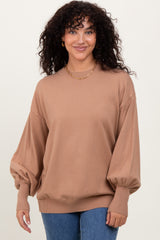 woman wearing a brown oversized sweater with balloon sleeves, styled with blue jeans and a gold chain necklace