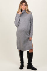 woman wearing a grey turtleneck maternity sweater dress with side slits and knee-high black boots, showcasing her baby bump