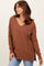 woman wearing a brown v-neck oversized sweater with side slits, styled with blue jeans and a chunky necklace
