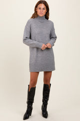 woman wearing a gray turtleneck sweater dress and black knee-high patent leather boots