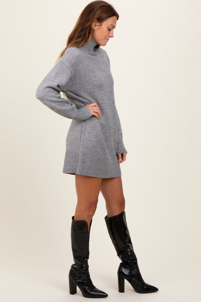 woman wearing a gray knit sweater dress with a high neck and side slits, paired with black knee-high heeled boots