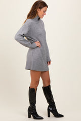 woman wearing a gray knit sweater dress with a high neck and side slits, paired with black knee-high heeled boots