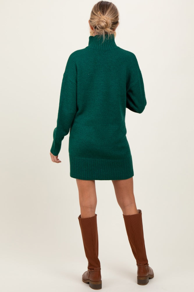 woman wearing a green maternity sweater dress with a high neck and ribbed hem, showing off a baby bump