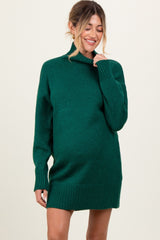 woman wearing a dark green oversized maternity sweater dress with a mock neck and ribbed detailing, showing her baby bump