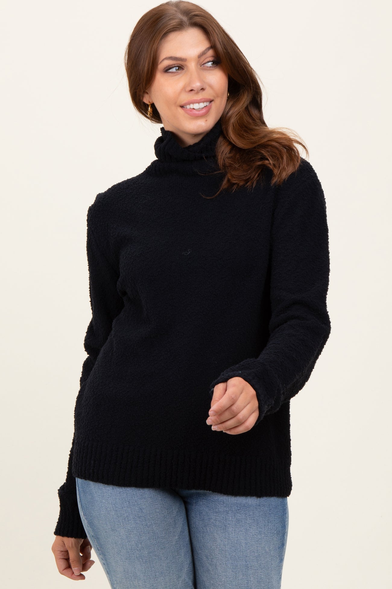 woman wearing a black cozy sweater with a high neckline and ribbed hem, paired with light blue jeans