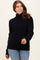 woman wearing a black cozy sweater with a high neckline and ribbed hem, paired with light blue jeans