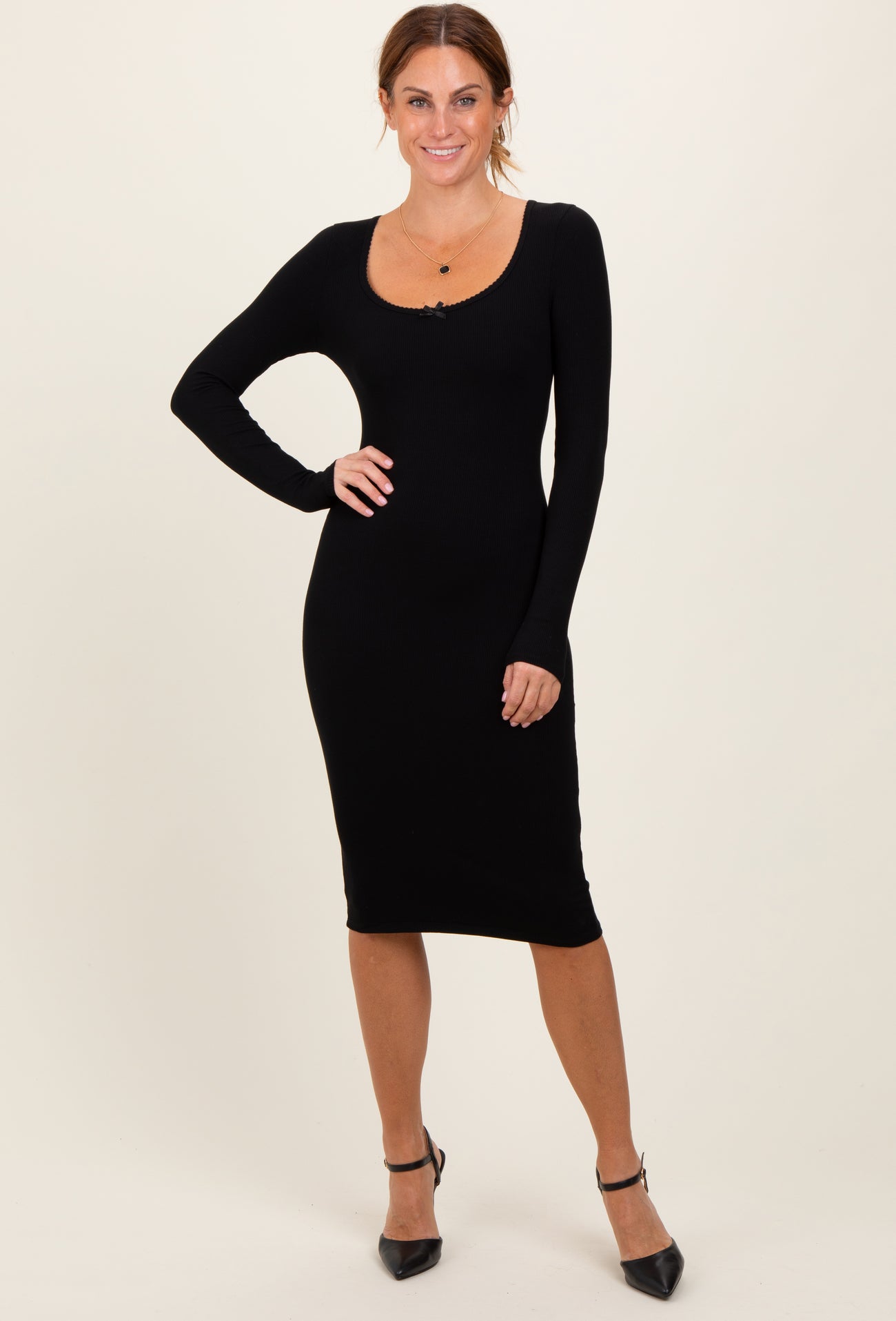 woman wearing a black ribbed long sleeve midi dress with a scoop neckline and posing elegantly