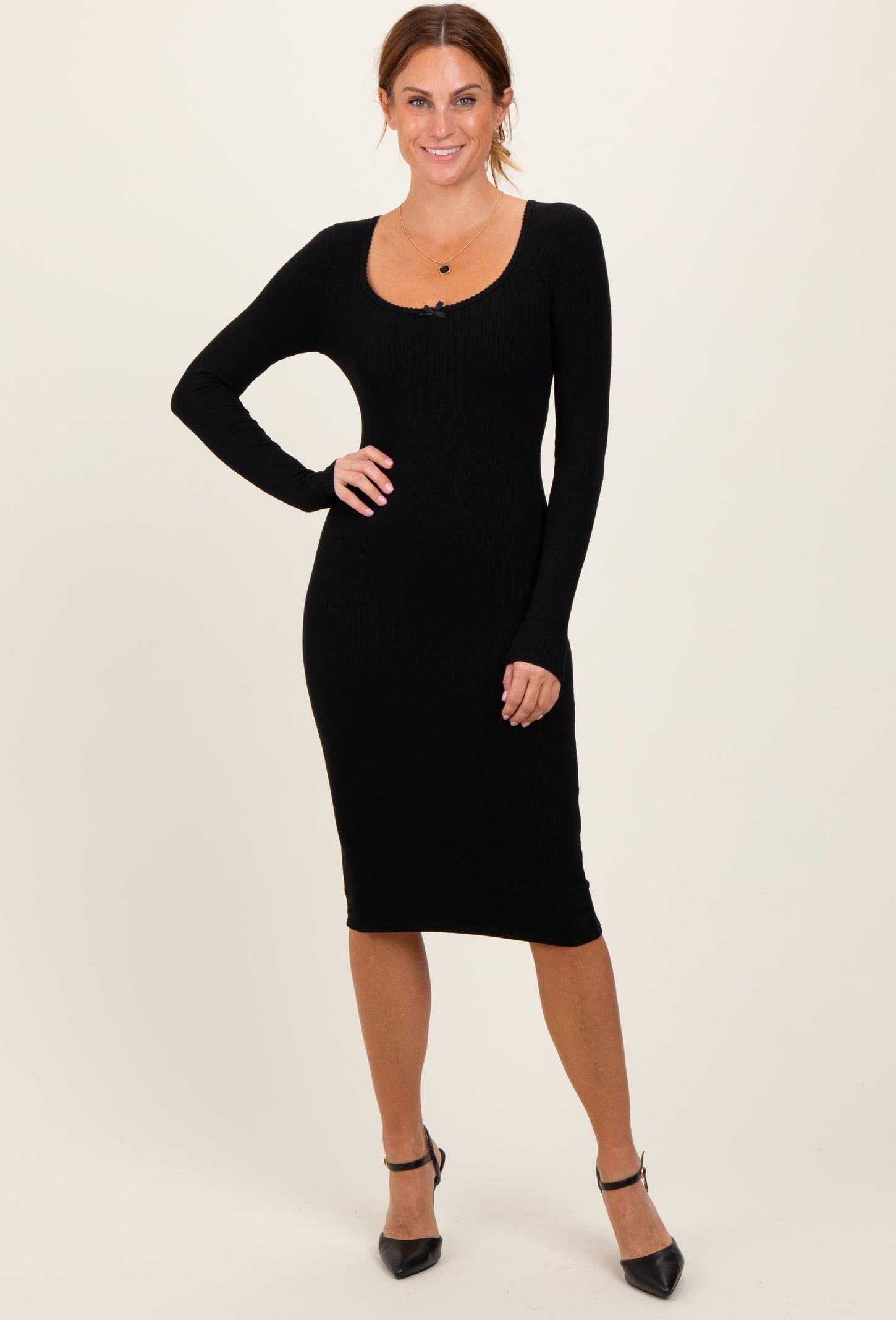 woman wearing a black ribbed long sleeve midi dress with a scoop neckline and posing elegantly