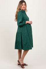 woman wearing a dark green maternity dress with long sleeves and a tiered skirt, showing her baby bump