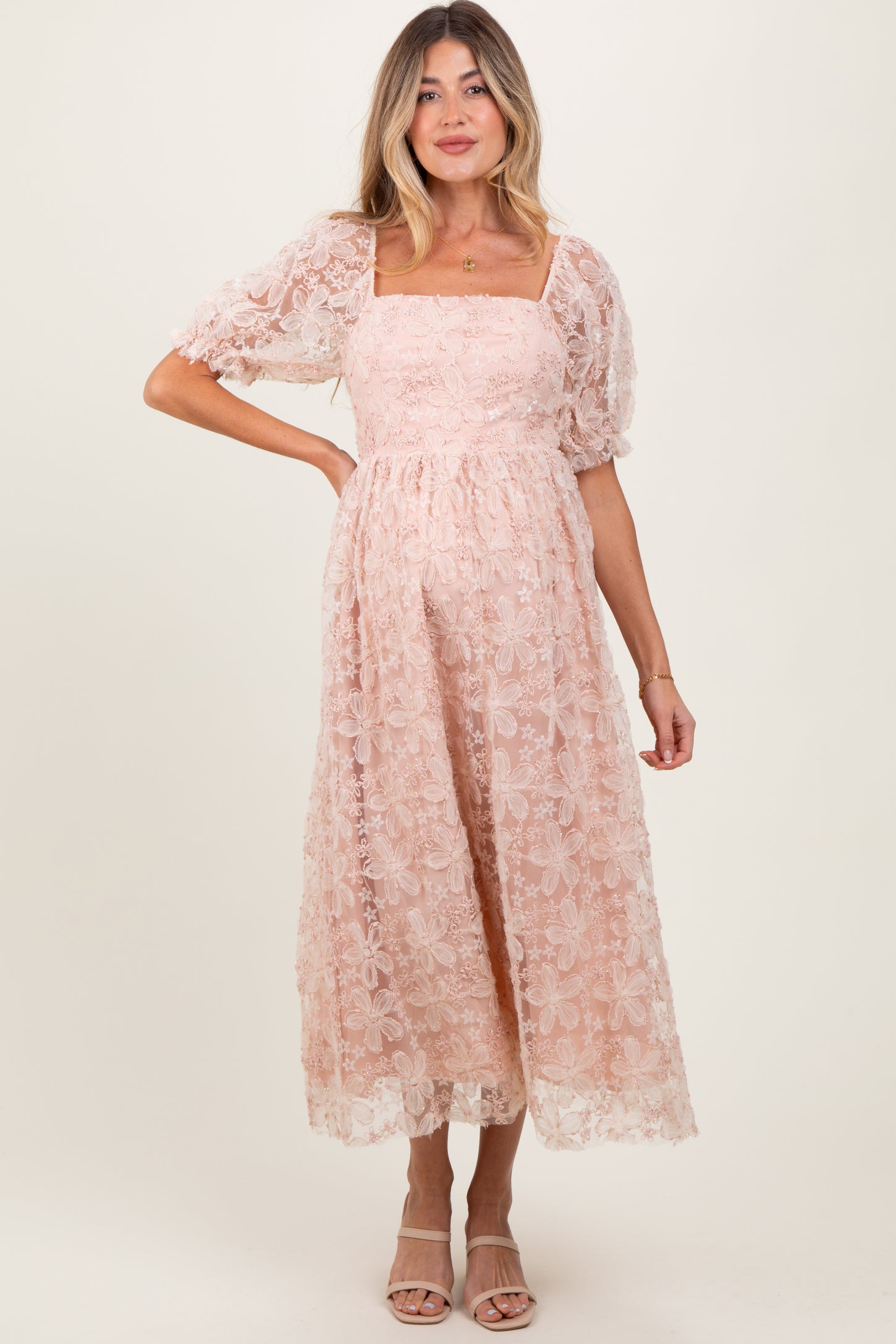 woman wearing a blush pink floral lace maternity dress with puff sleeves and a square neckline, showing her baby bump