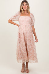 woman wearing a blush pink floral lace maternity dress with puff sleeves and a square neckline, showing her baby bump