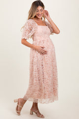 woman wearing a blush pink lace maternity dress with short puff sleeves and holding her baby bump