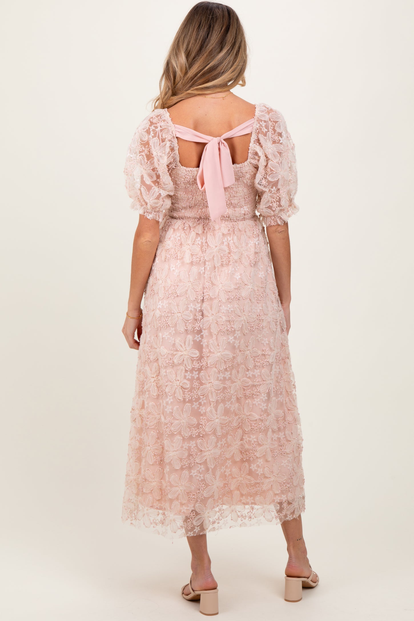 woman wearing a pink lace maternity dress with puff sleeves and a tie back, showing a gathered waist and floral design
