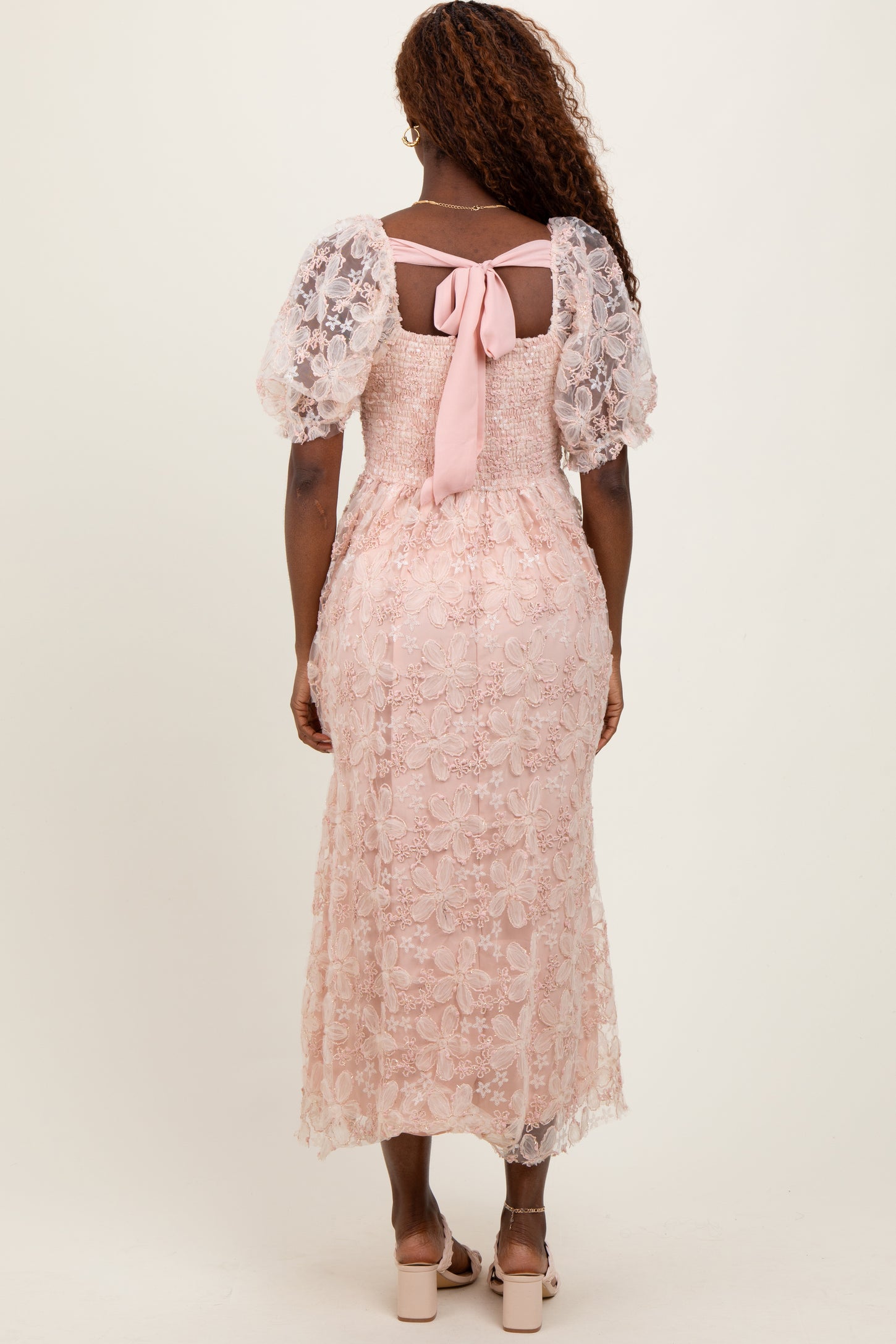woman wearing a pink floral lace midi dress with puff sleeves and a bow detail at the back