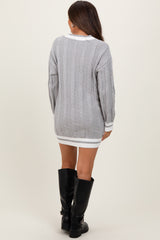 woman wearing a gray cable knit maternity sweater dress with white trim and knee-high black boots, baby bump not visible