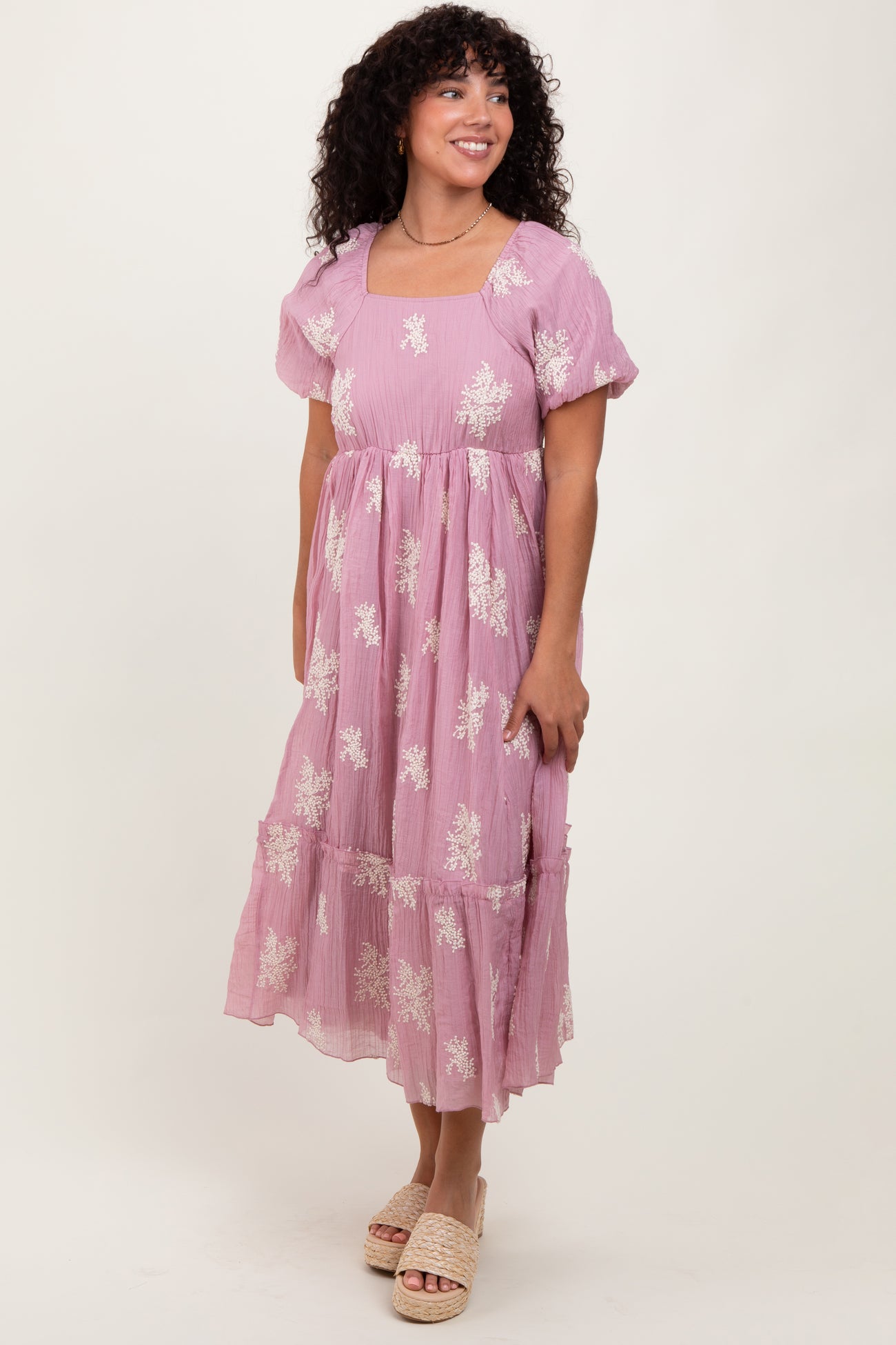 woman wearing a lavender midi dress with white floral embroidery and short puff sleeves, standing on a neutral background
