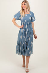 woman wearing a blue embroidered midi dress with puff sleeves and a tiered skirt