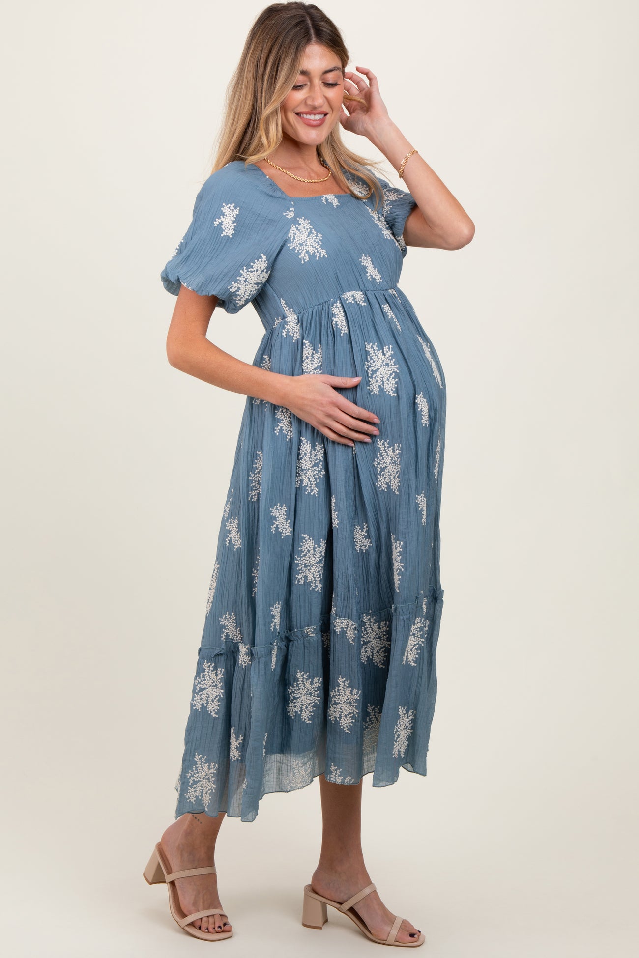 woman wearing a blue maternity maxi dress with floral patterns, cradling her baby bump