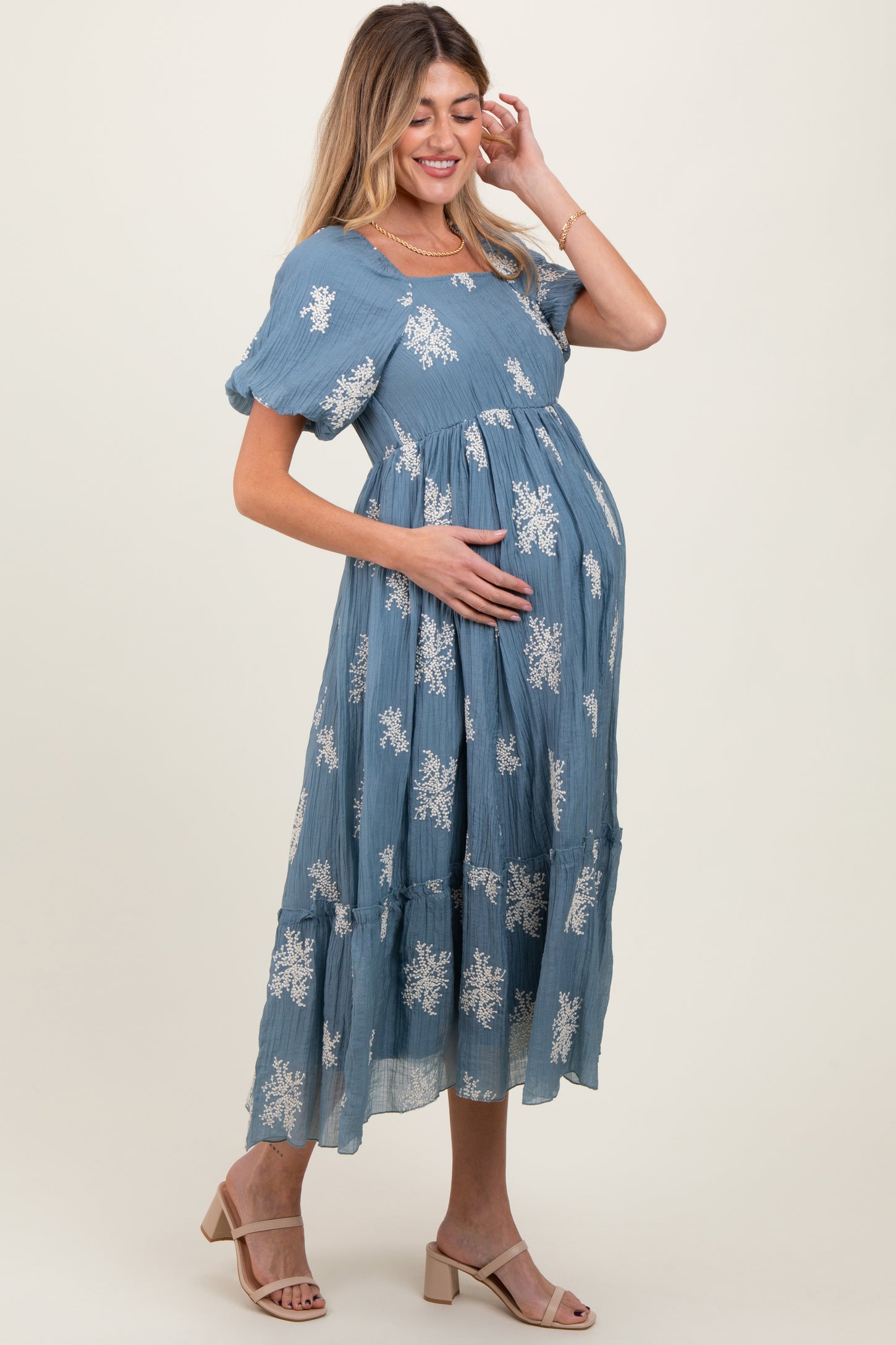 woman wearing a blue maternity maxi dress with floral patterns, cradling her baby bump