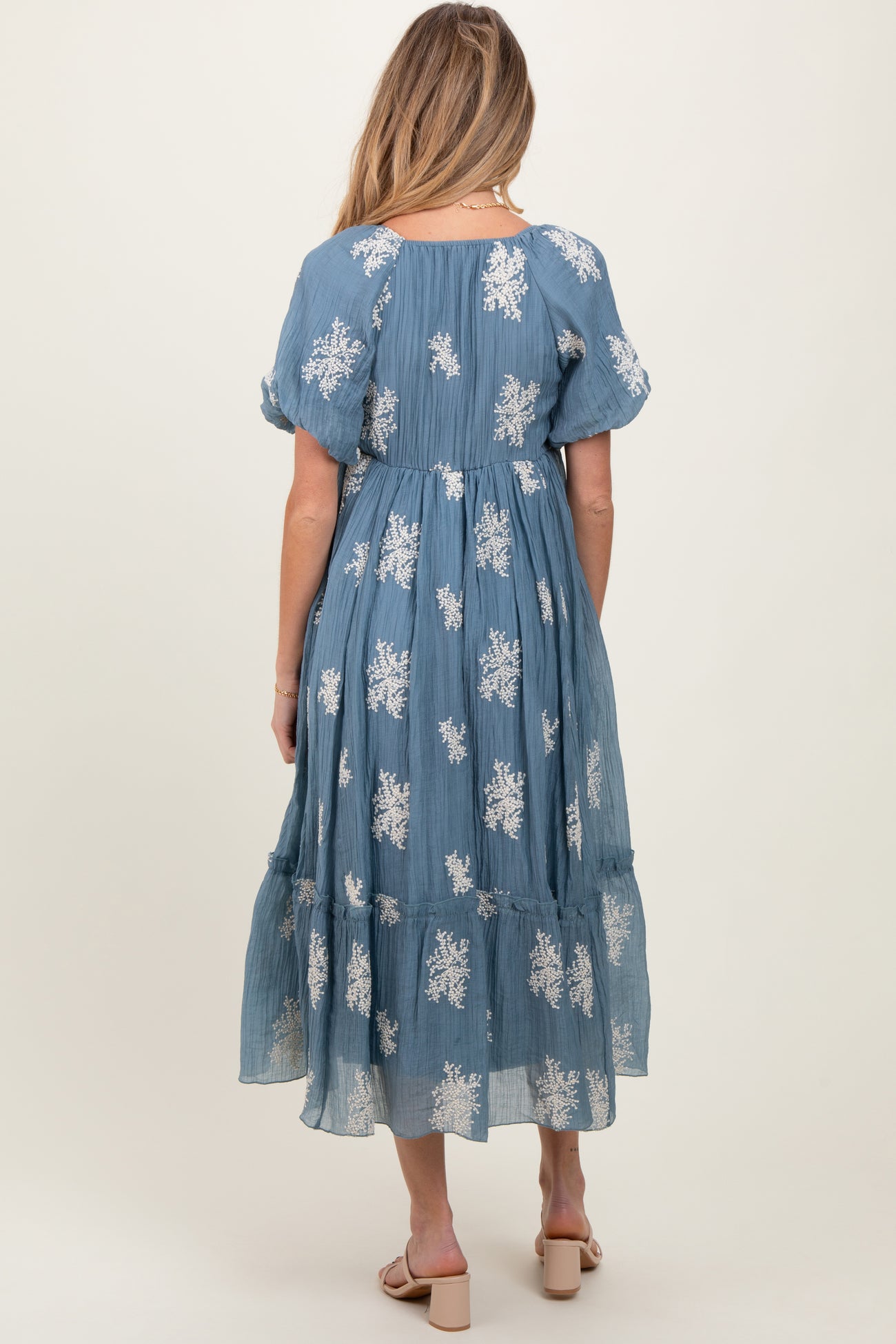 woman wearing a blue floral print maternity dress with puff sleeves and a tiered skirt, showing a baby bump
