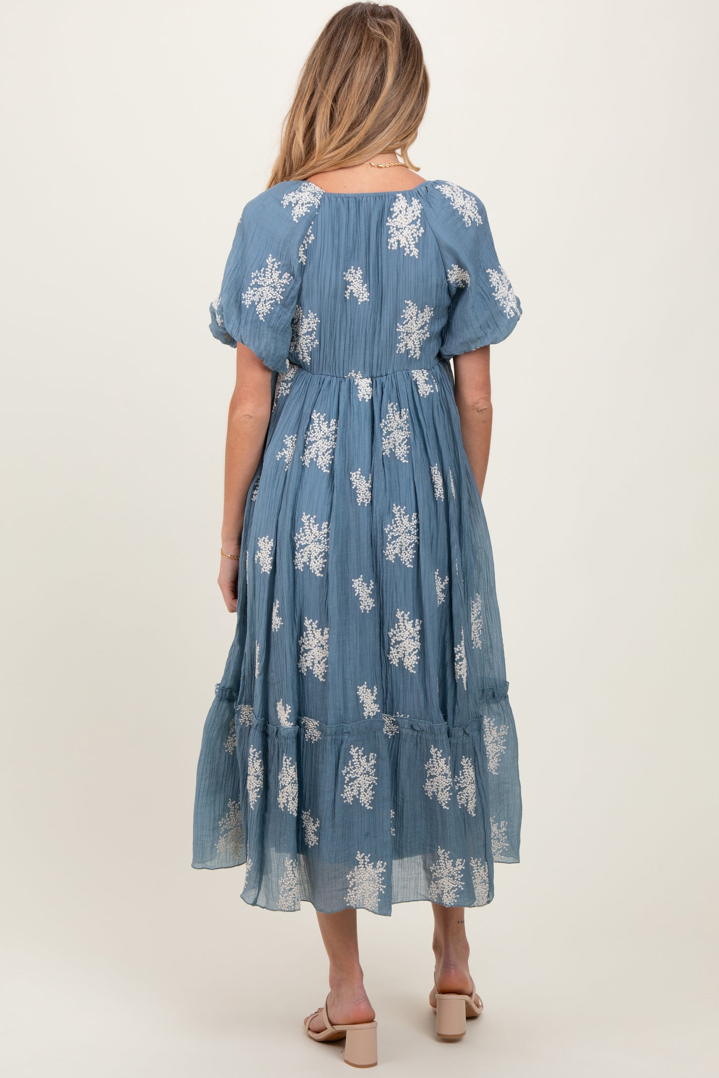 woman wearing a blue floral print maternity dress with puff sleeves and a tiered skirt, showing a baby bump
