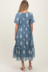 woman wearing a blue floral print maternity dress with puff sleeves and a tiered skirt, showing a baby bump