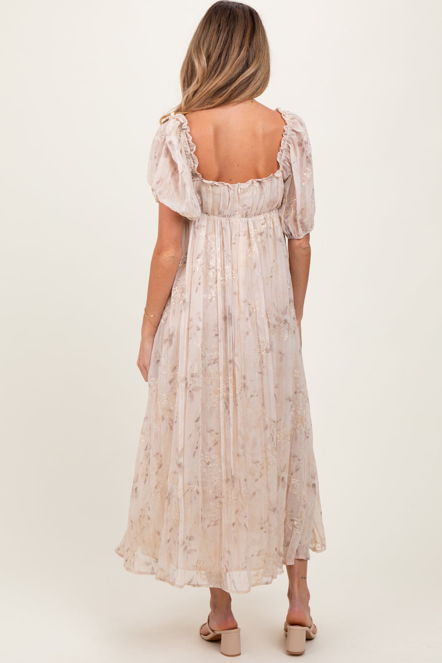 woman wearing a light pink floral maternity maxi dress with puff sleeves, showing a relaxed fit from the back