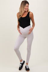 woman wearing a black tank top and light gray maternity leggings, showing her baby bump while smiling