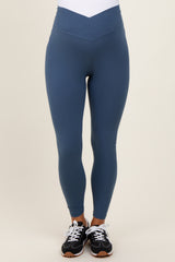 woman wearing blue maternity leggings with a v-shaped waistband and paired with black athletic shoes