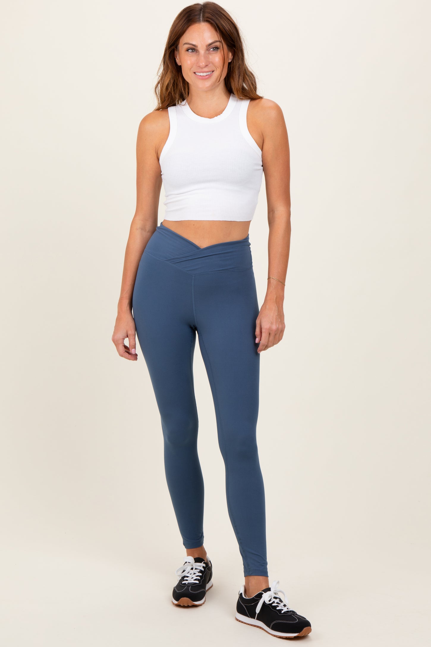 woman wearing a white ribbed crop top and teal high-waisted leggings, posing with a smile