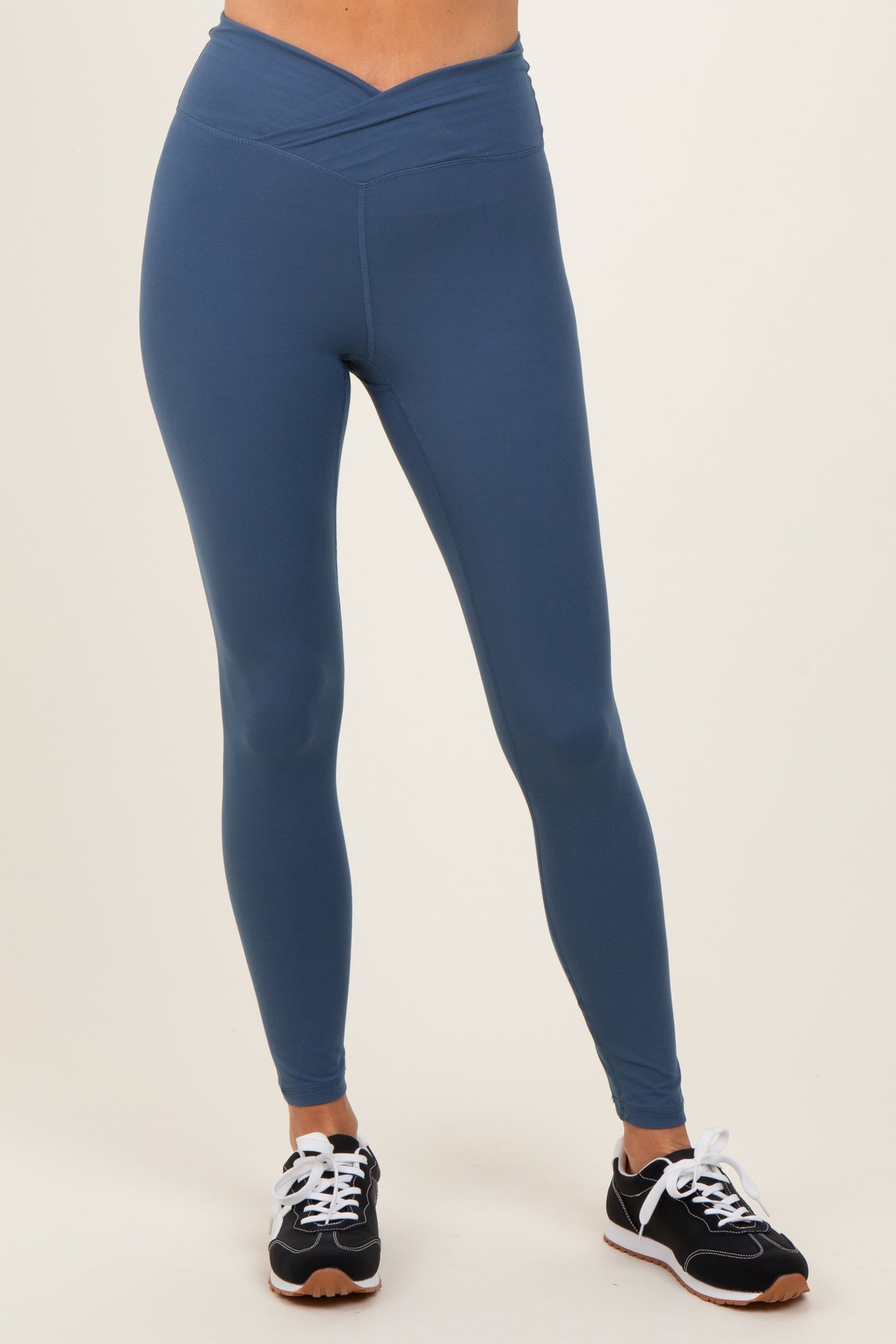 woman wearing dark blue high-waisted leggings with a crossover waistband and black athletic shoes