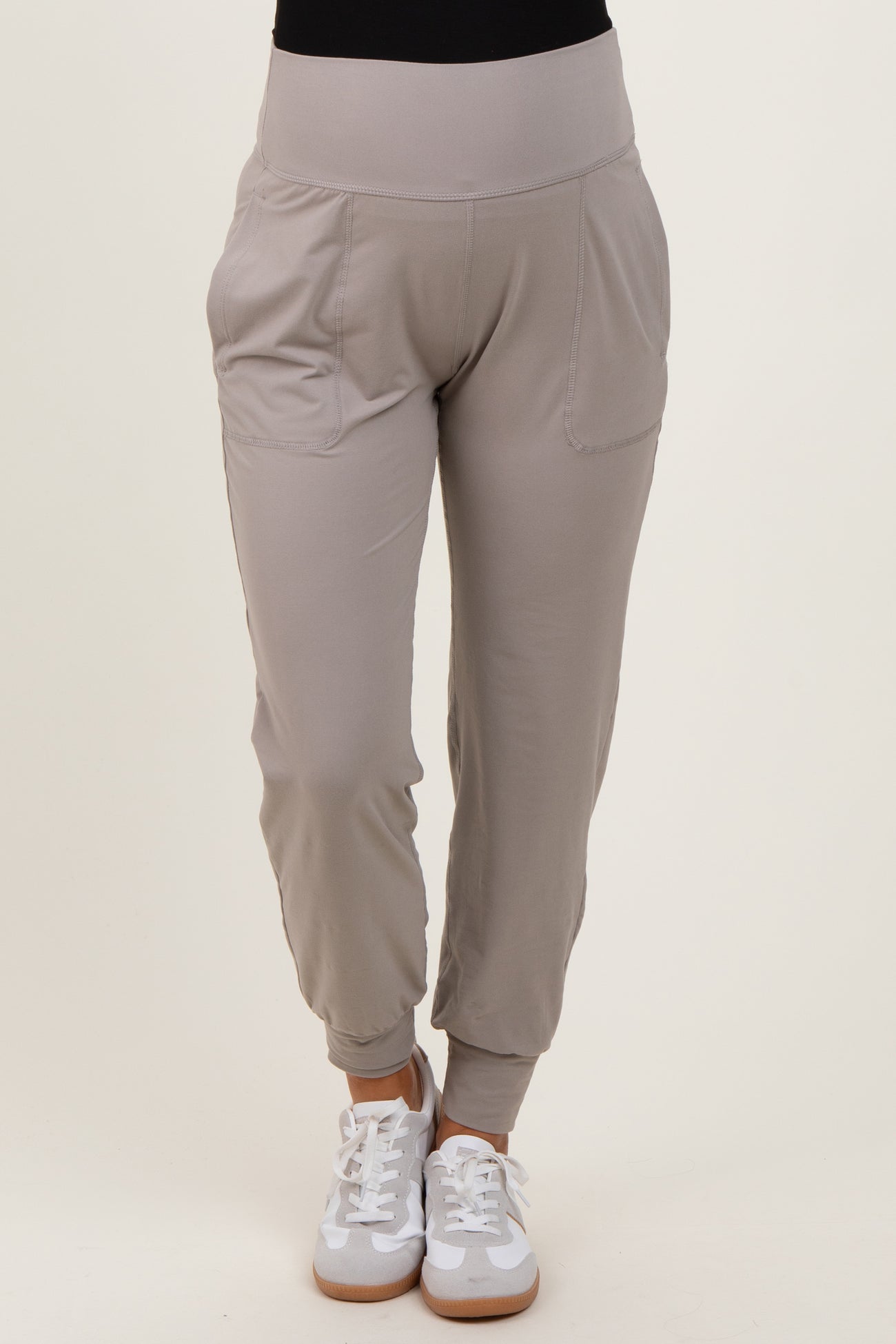 woman wearing light grey maternity jogger pants with side pockets and elastic waistband, paired with white sneakers
