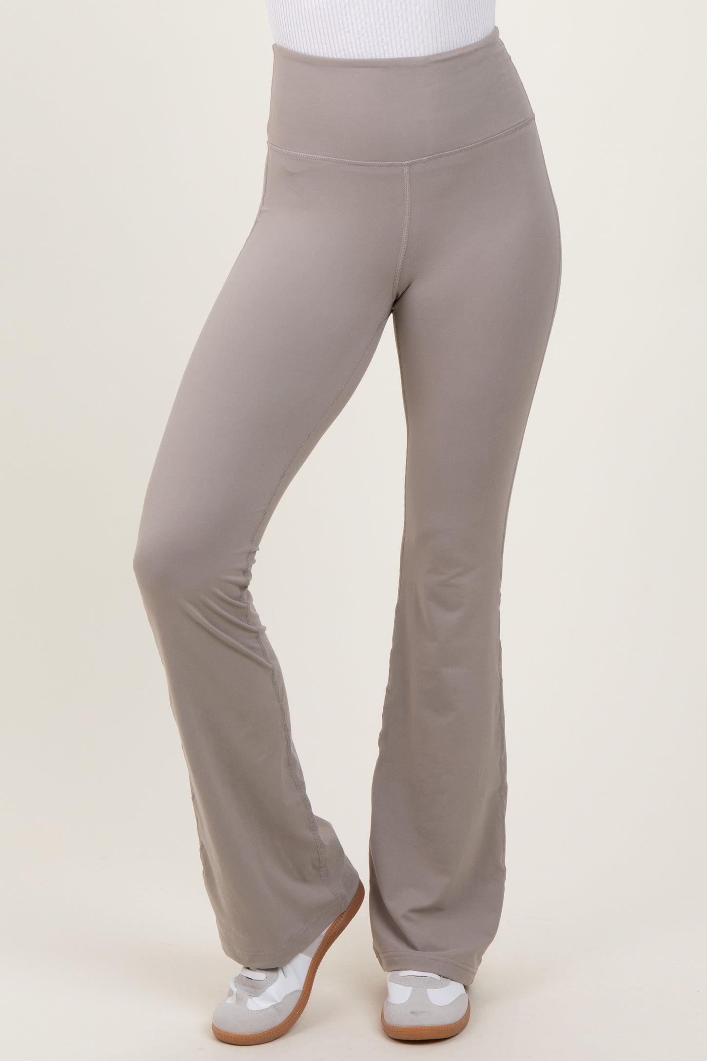 woman wearing light gray flared workout pants with a high waistband and paired with white sneakers
