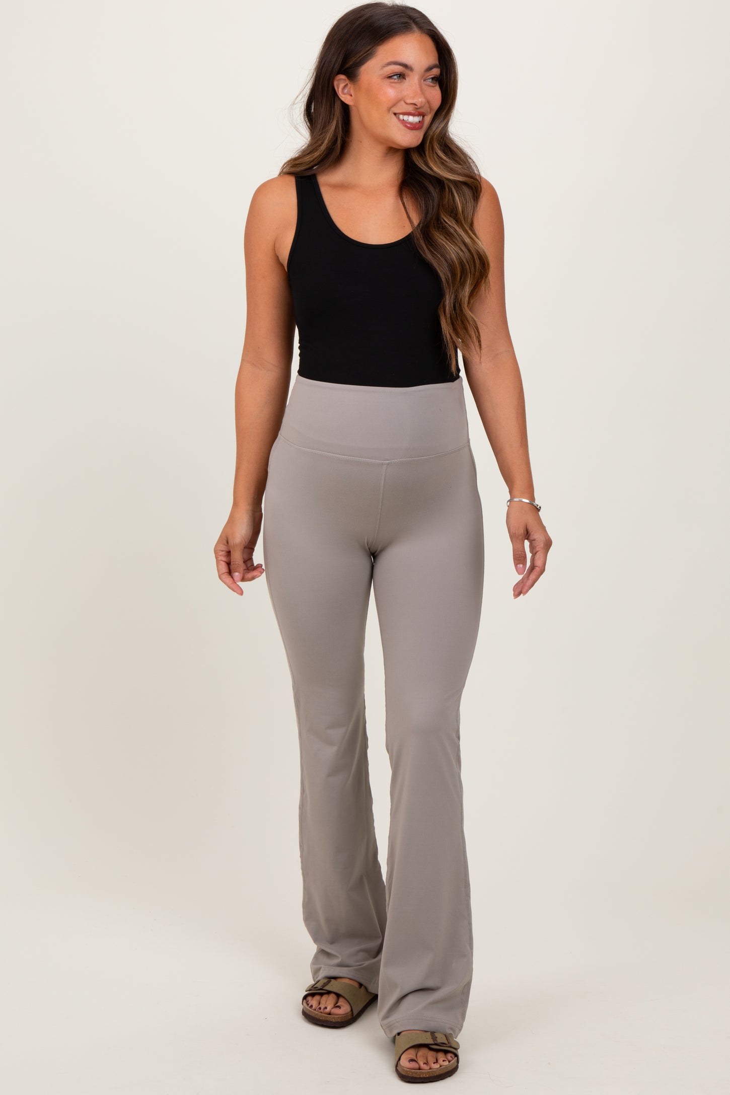 woman wearing a black tank top and taupe maternity flared leggings with a supportive waistband