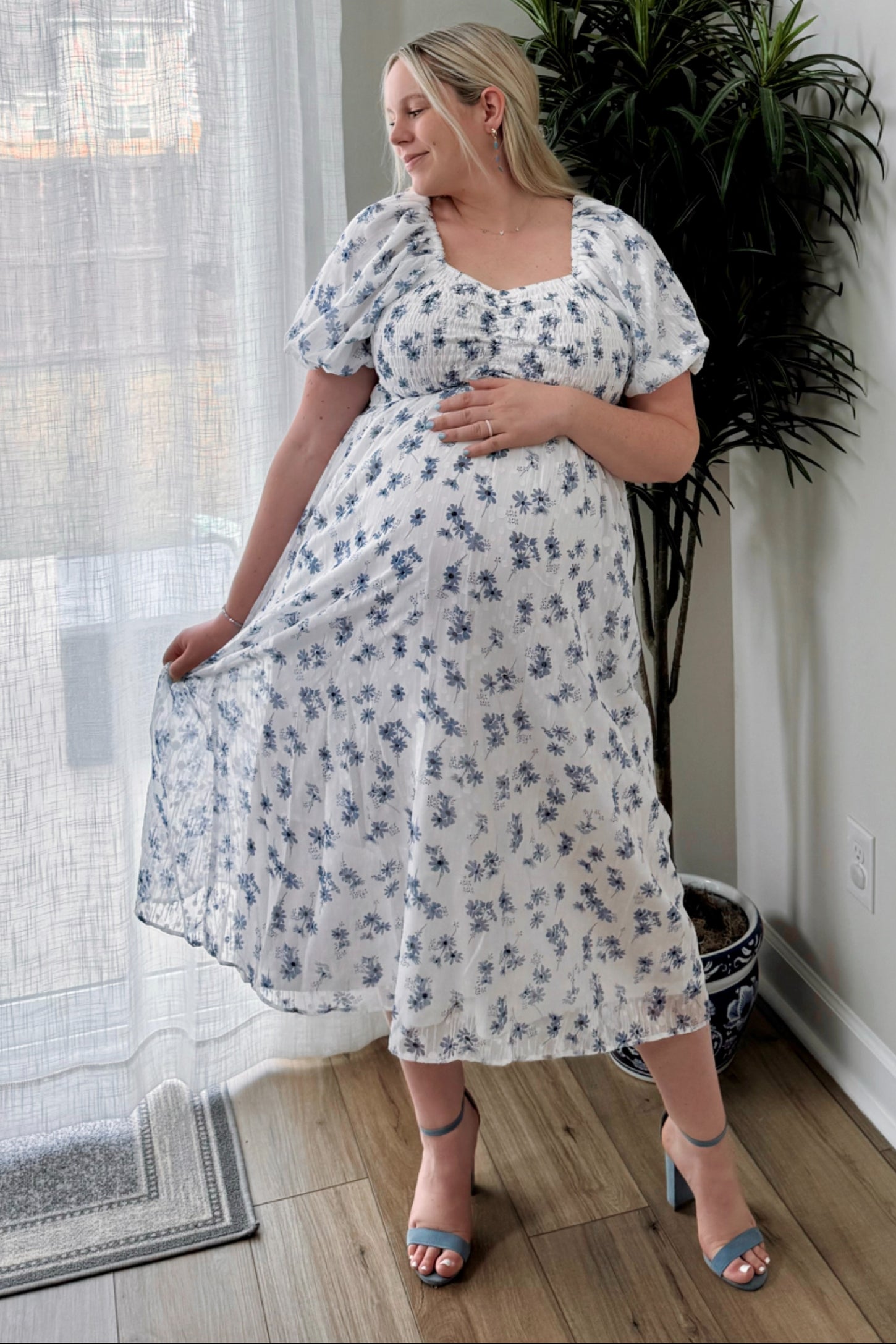 woman wearing a floral maternity dress with short puff sleeves and a flowing skirt, showing her baby bump