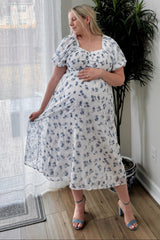 woman wearing a floral maternity dress with short puff sleeves and a flowing skirt, showing her baby bump