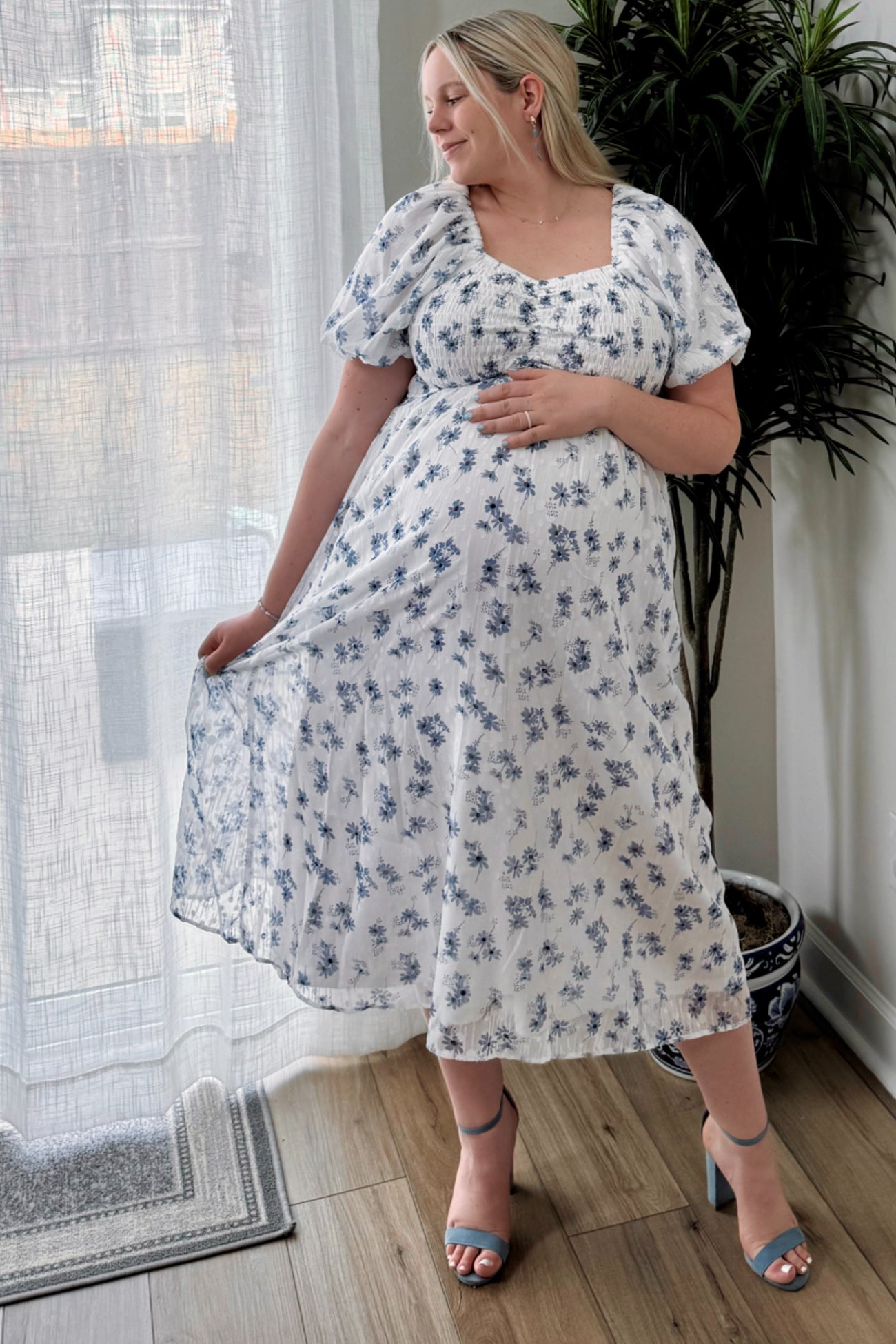 woman wearing a white floral maternity dress with short puff sleeves and holding her baby bump